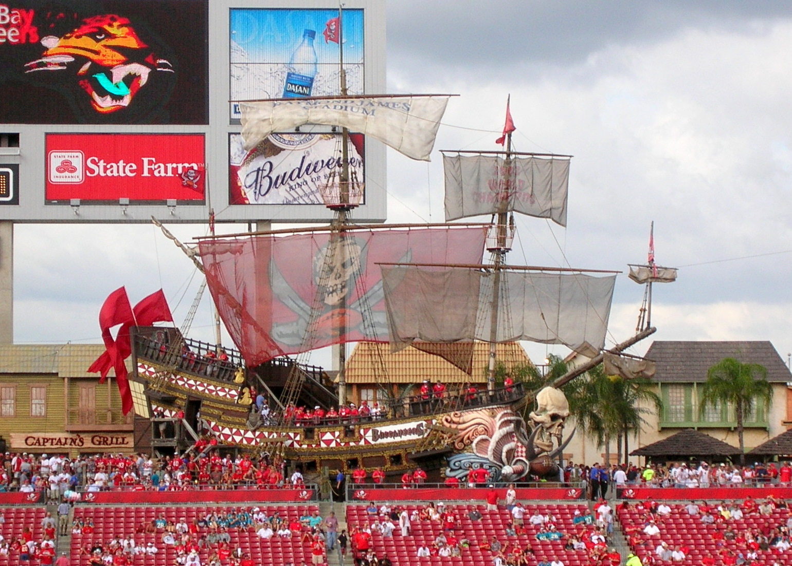 The full-size pirate ship in Buccaneer Cove at Raymond James Stadium, with red sails and a skull figurehead, above the stadium seating