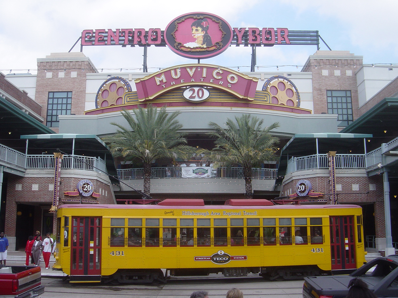 The Centro Ybor entertainment complex with its large sign above a cinema marquee, and a yellow and red TECO Line streetcar passing in front