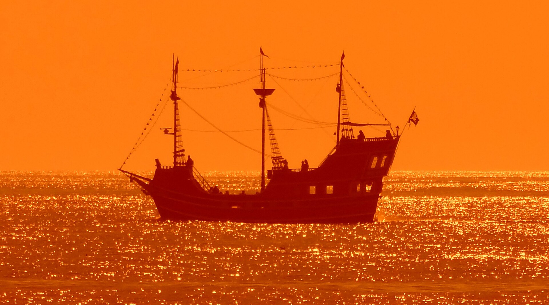 A three-masted tourist pirate ship silhouetted black against a brilliant orange Gulf of Mexico sunset off Clearwater Beach, its rigging sharp against the sky