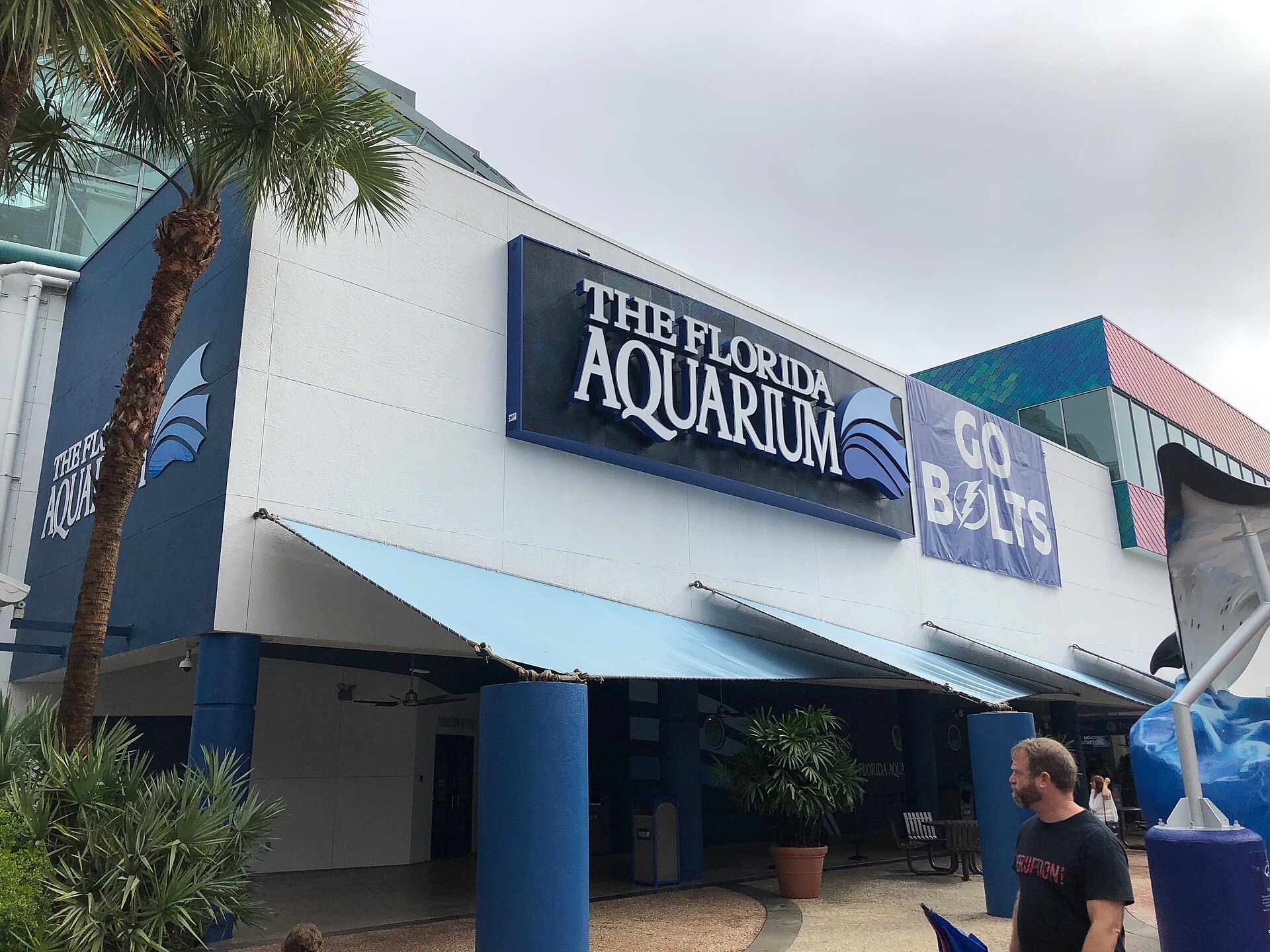 The entrance to The Florida Aquarium in Tampa, with its name on the facade above a shaded canopy and palm trees in front
