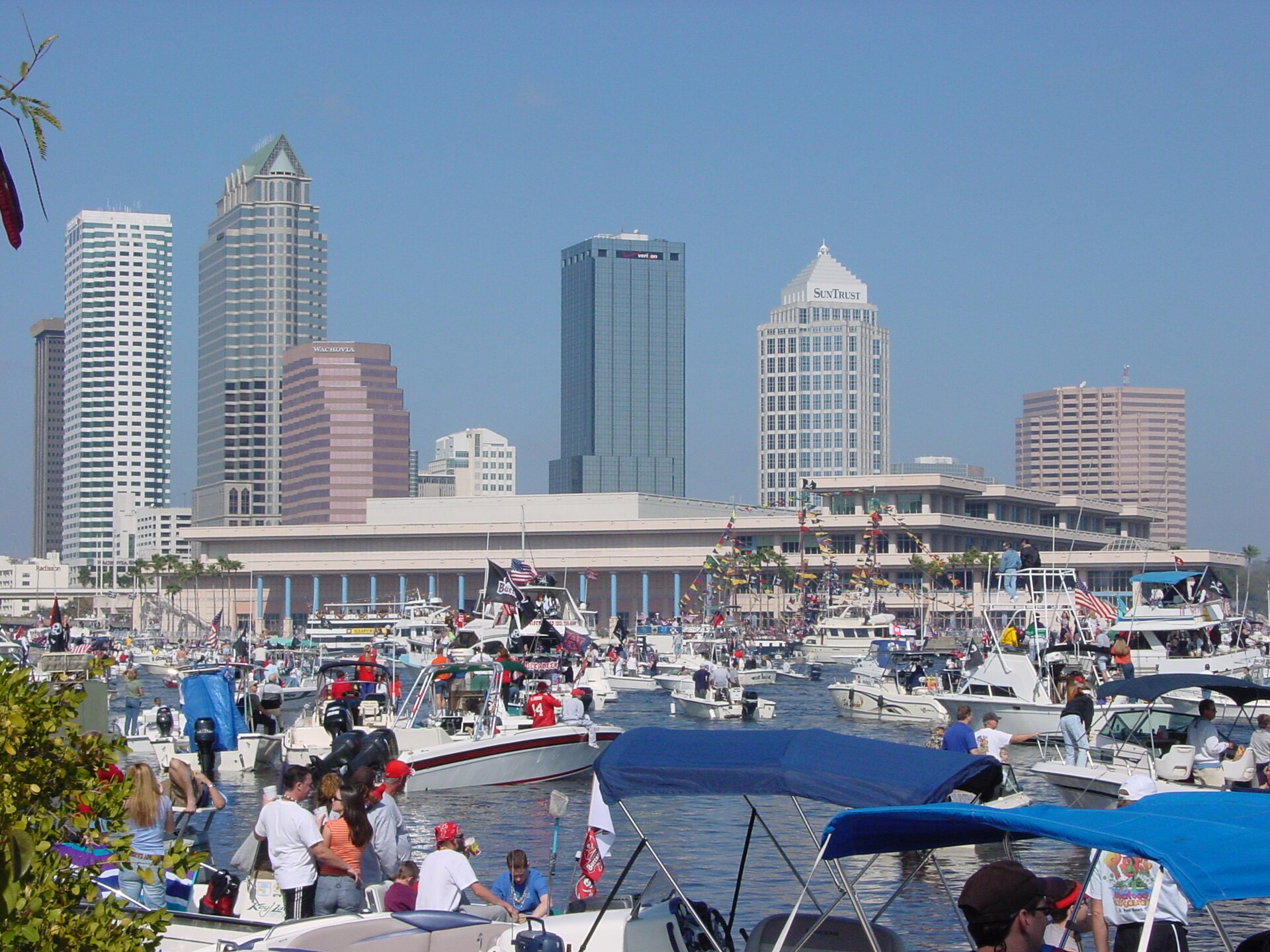 Hundreds of private boats flying pirate flags packed into the channel beside the Tampa Convention Center during Gasparilla, with the downtown skyline behind
