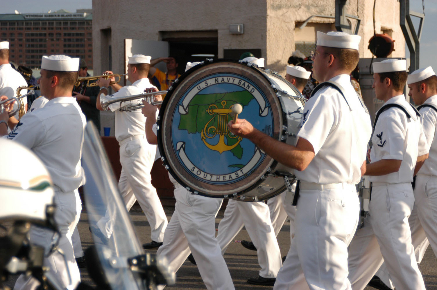 A US Navy marching band in white uniforms playing trumpets and a bass drum while marching in Tampa's Gasparilla parade