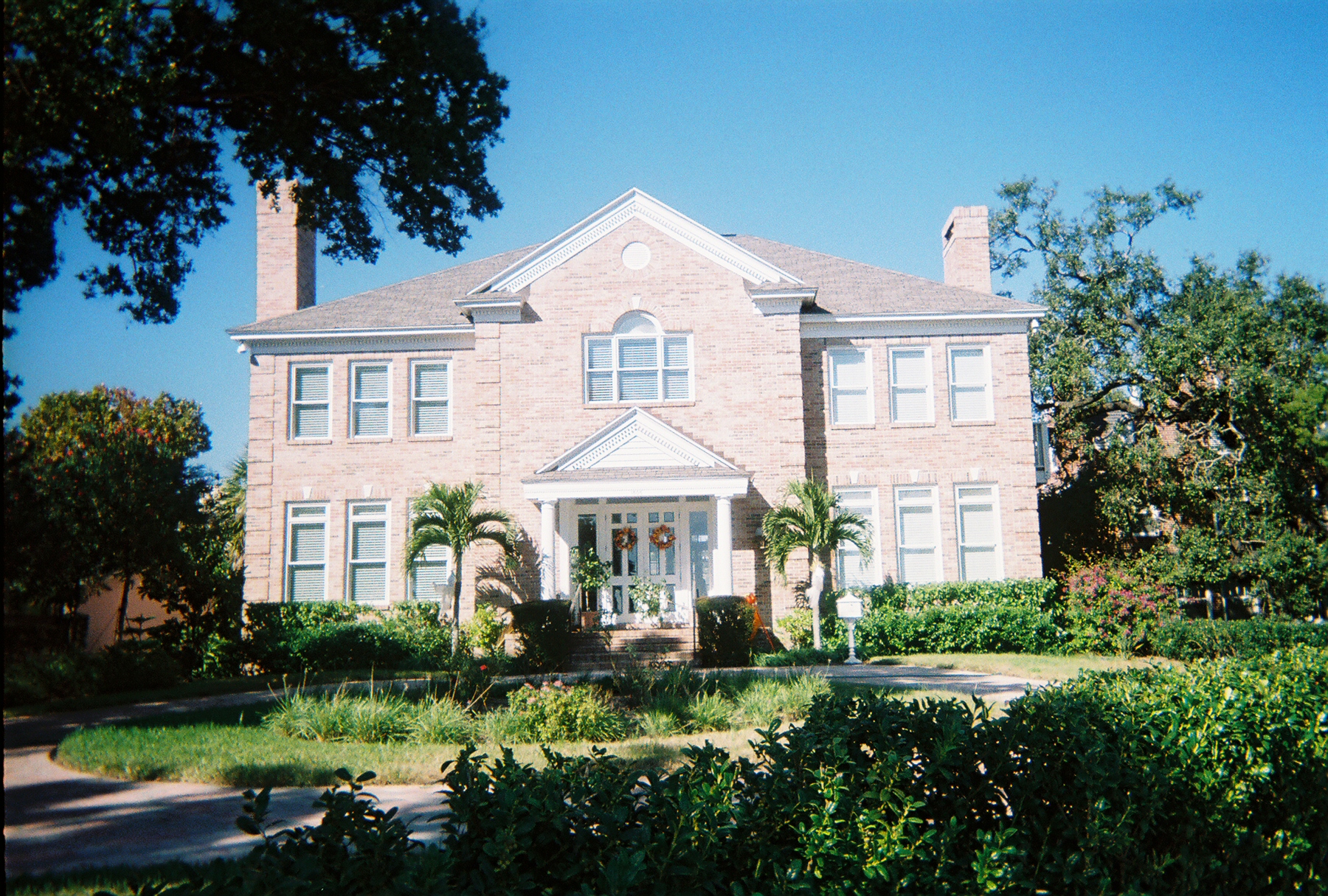 A two-storey brick colonial revival house with white columns and a pedimented porch, set behind palms and hedges in the Hyde Park Historic District of Tampa