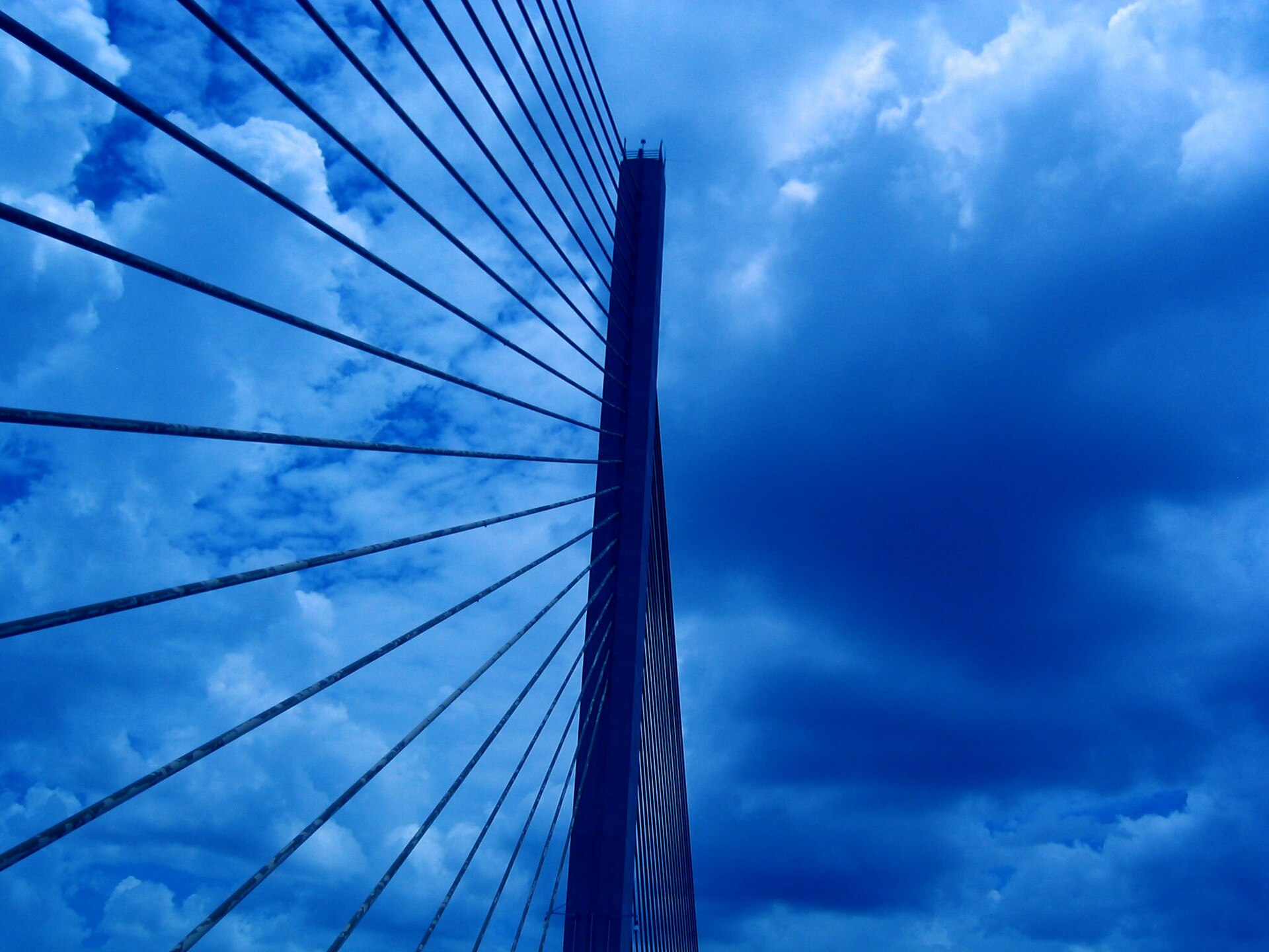 Looking steeply up at the cable-stayed pylon of the Sunshine Skyway Bridge, its fan of steel cables radiating out against a deep blue sky