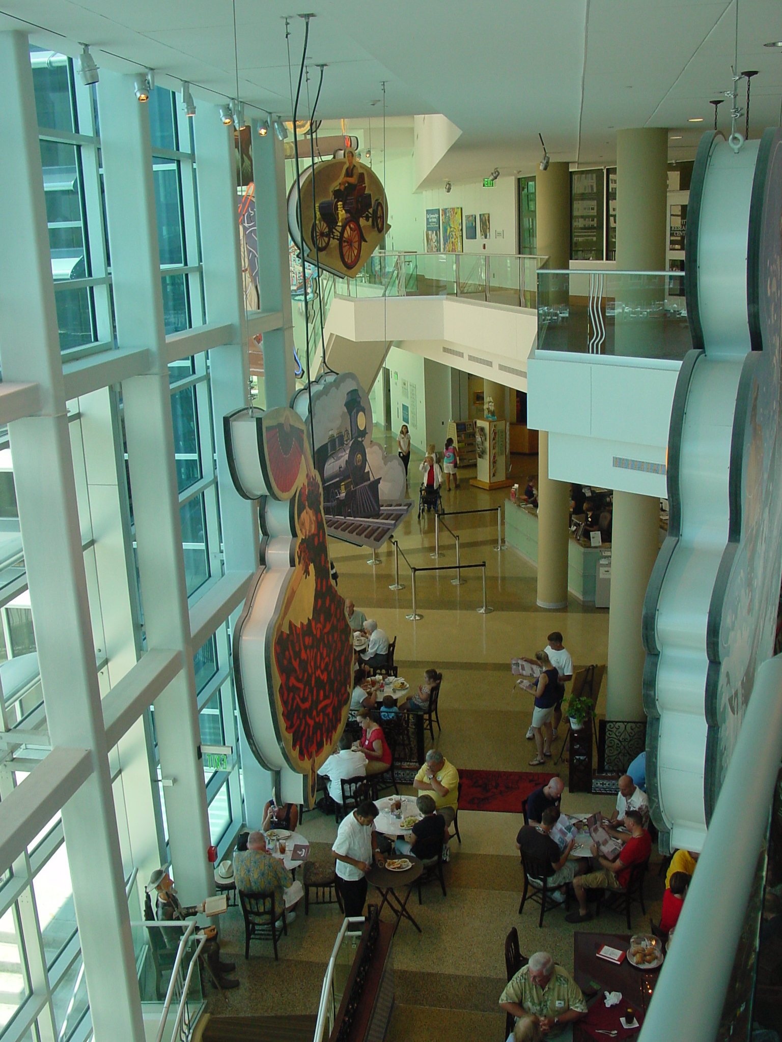 Looking down into the tall glass-walled atrium of the Tampa Bay History Center, with hanging cigar-label artwork above a cafe where people are dining at tables