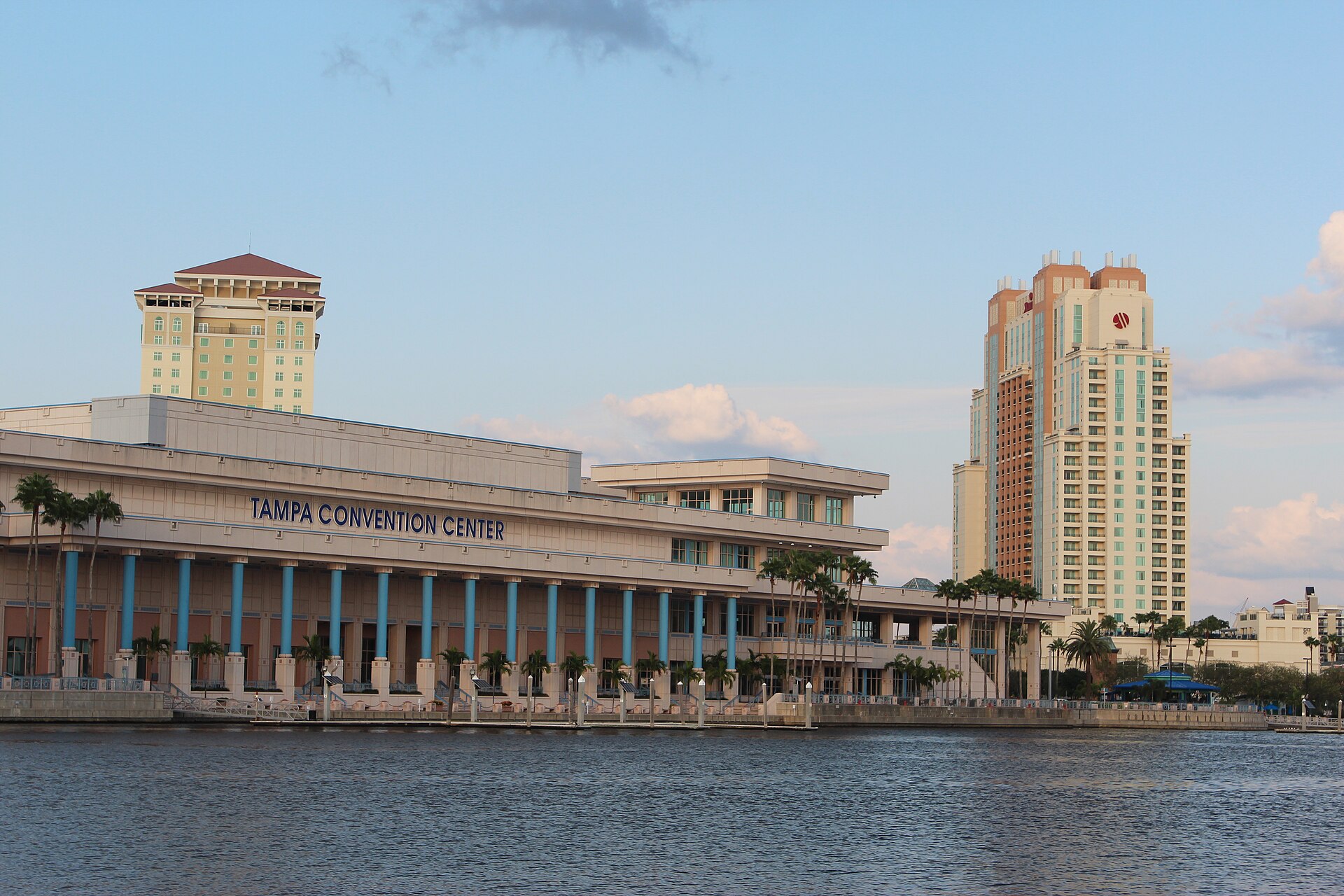 The Tampa Convention Center seen across the water at dusk, with downtown hotel towers behind it
