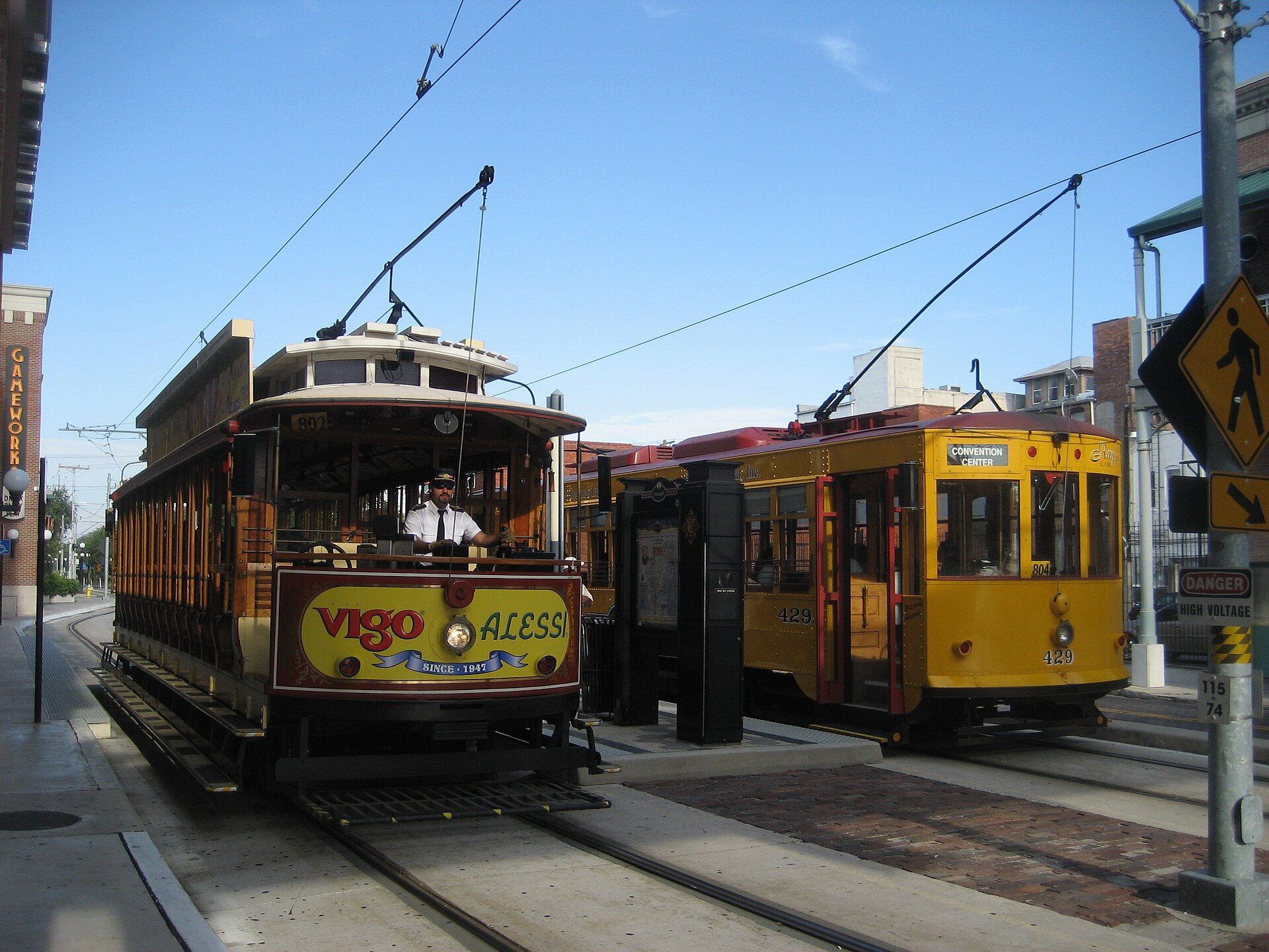 Two restored yellow TECO Line streetcars at a station in Ybor City, one displaying a Convention Center destination sign