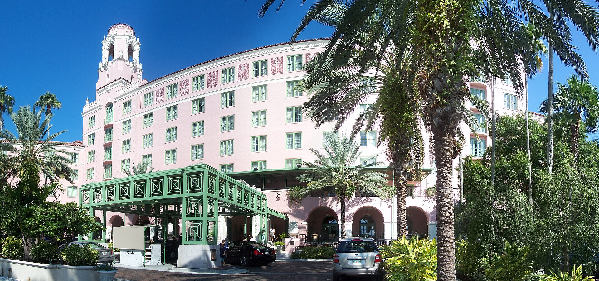 The pink Mediterranean Revival facade and bell tower of the Vinoy in downtown St. Petersburg, with a green iron porte-cochere and tall palm trees in front