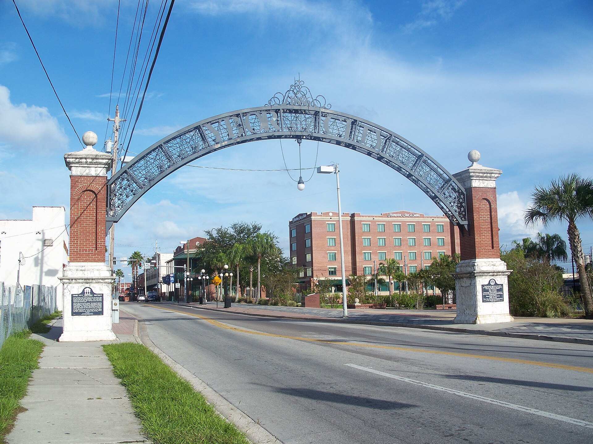 The wrought-iron Ybor City arch spanning a street in Tampa's historic district, with a historical marker nearby