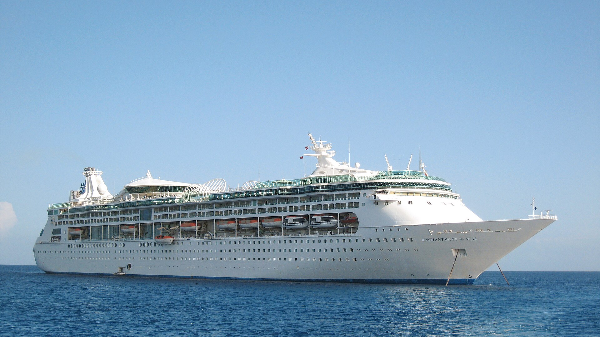 Royal Caribbean's Enchantment of the Seas at anchor in calm blue water under a clear sky, seen side-on from the water