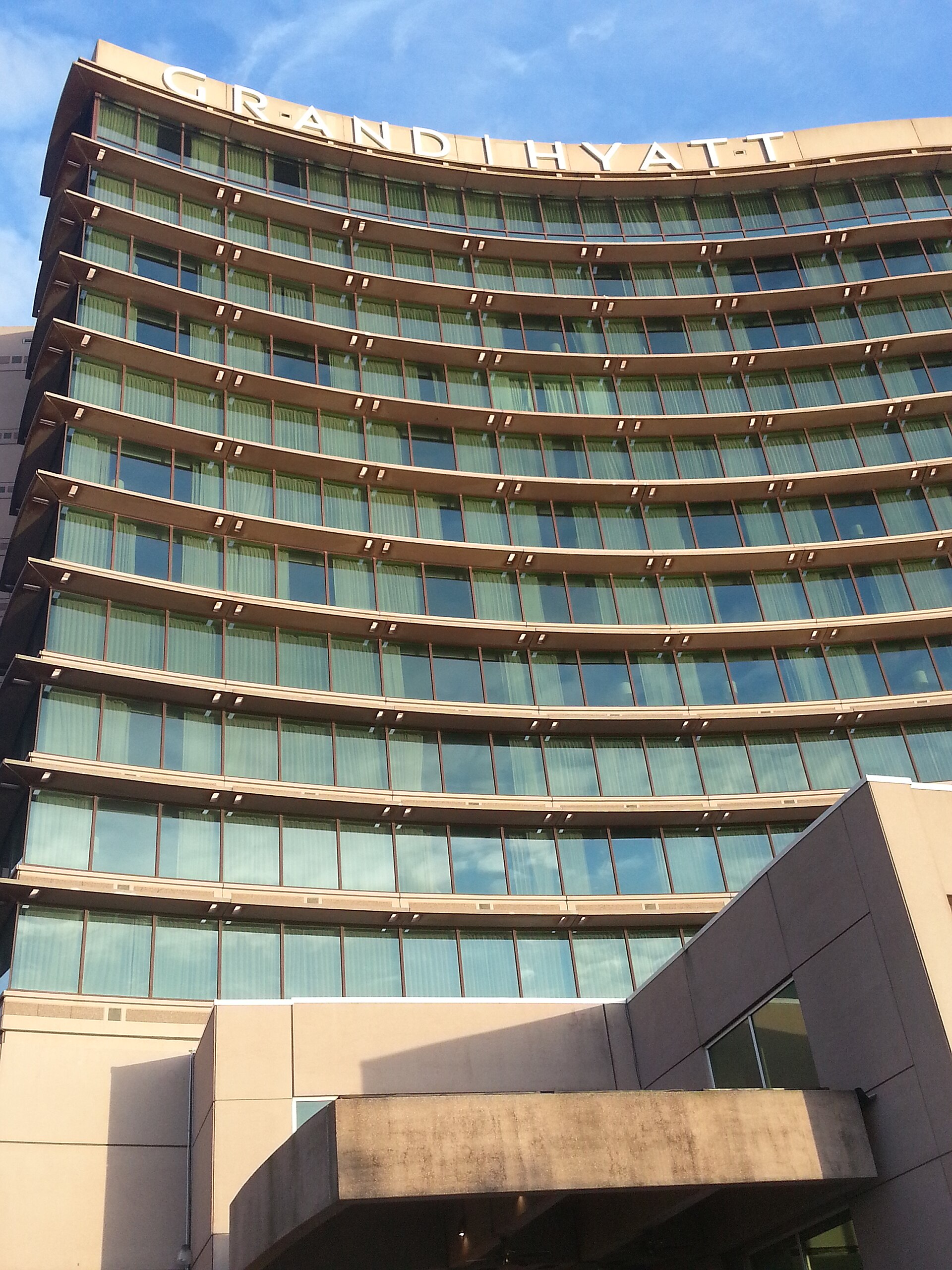 The curved, many-windowed tower of the Grand Hyatt Tampa Bay with the hotel's name across the top and the entrance canopy below