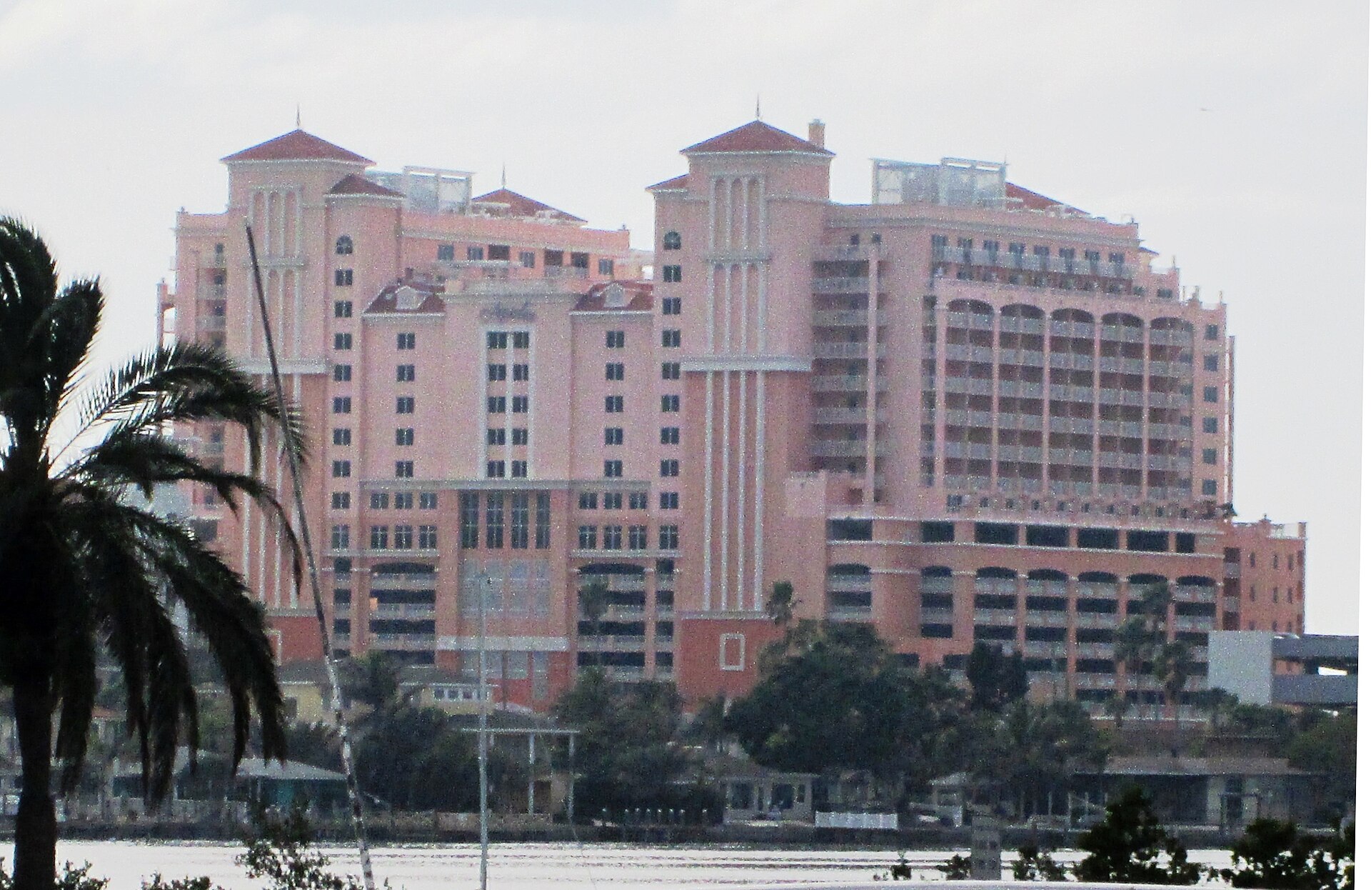 The pink towers of the Hyatt Regency Clearwater Beach Resort rising above trees and the waterfront, seen across the water from the Clearwater Marine Aquarium