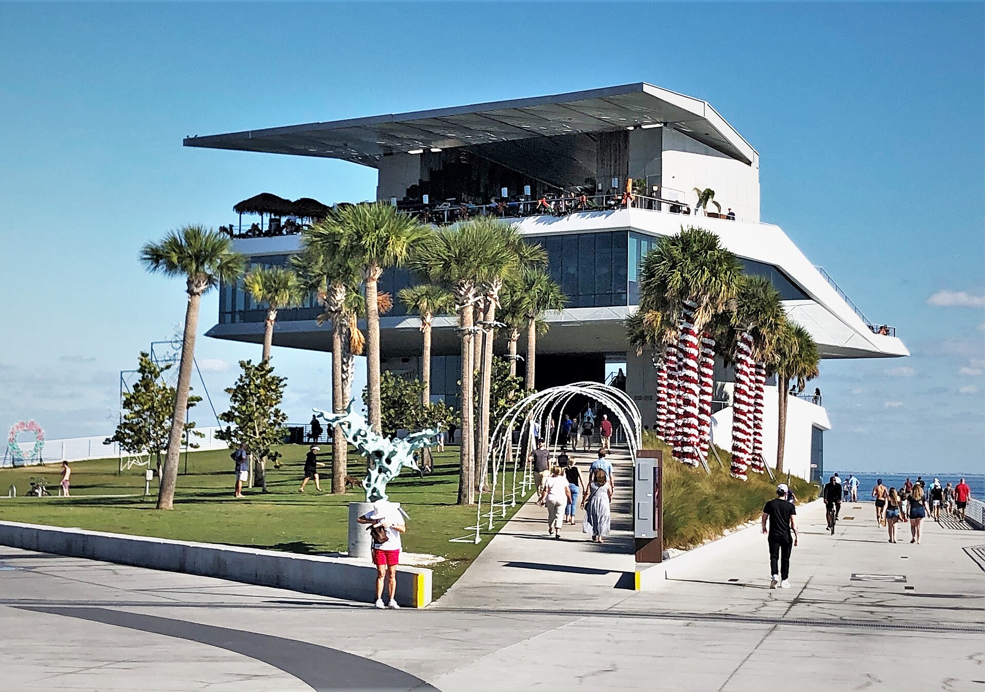 The Pier Point building at the end of the St. Pete Pier, a cantilevered white structure with a thatched rooftop bar, palm trees and people walking up the ramp beneath it