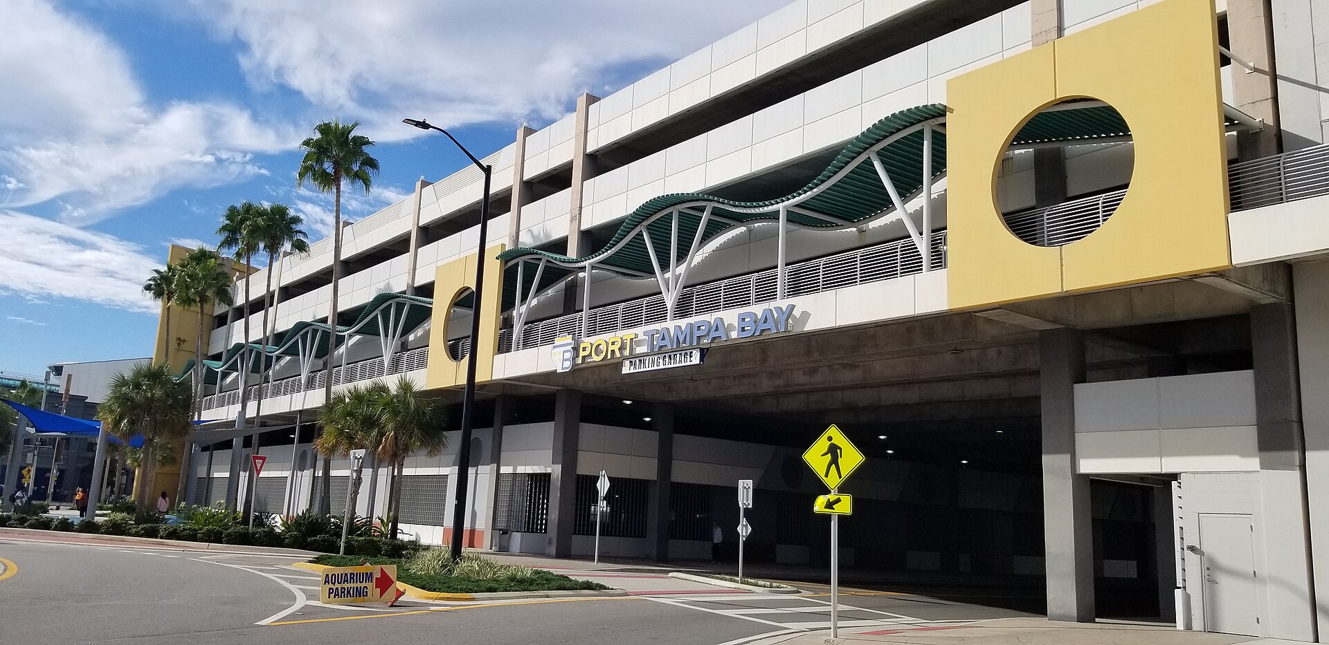 The Port Tampa Bay parking garage on Channelside Drive, a multi-story structure with yellow panels and green wave-shaped canopies, with a sign pointing to aquarium parking
